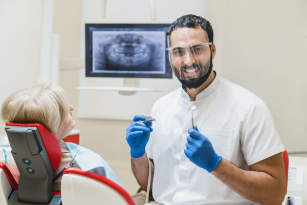 Middle-Eastern male smiling stomatologist dentist orthodontist looking at the camera curing healing female patient. Teeth tooth whitening, veneers implantation